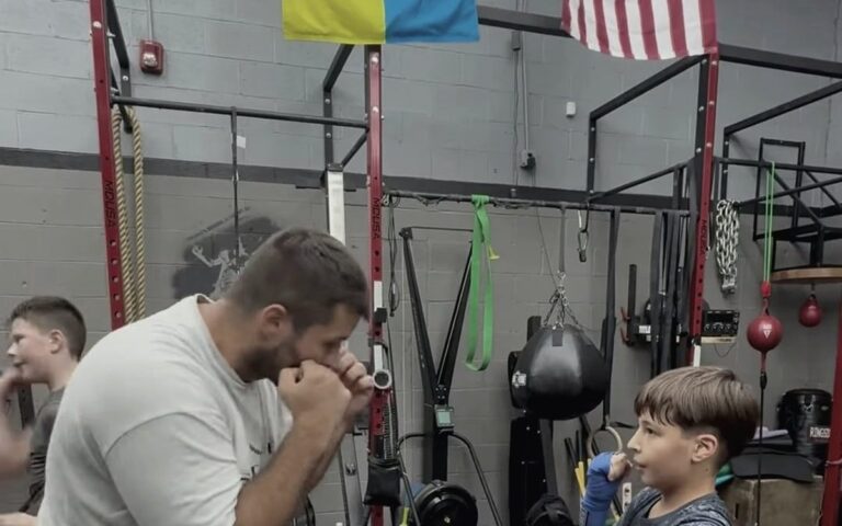 Coach showing a young boxer how to hold his guard, Ukrainian and US flags above